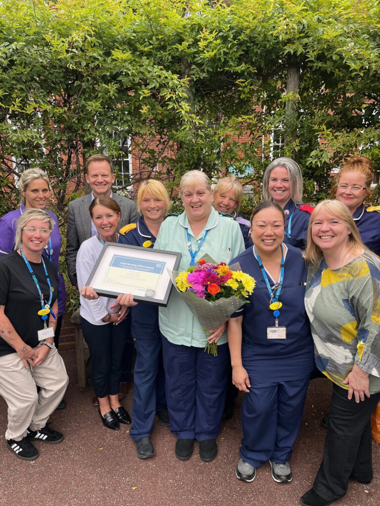 Healthcare support worker, Jacquie Betts, presented with award and flowers, surrounded by colleagues