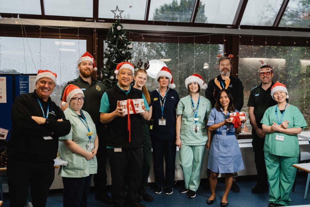Some of our colleagues at Torbay Hospital wearing Christmas hats and holding gifts, standing by the tree in Bayview restaurant.