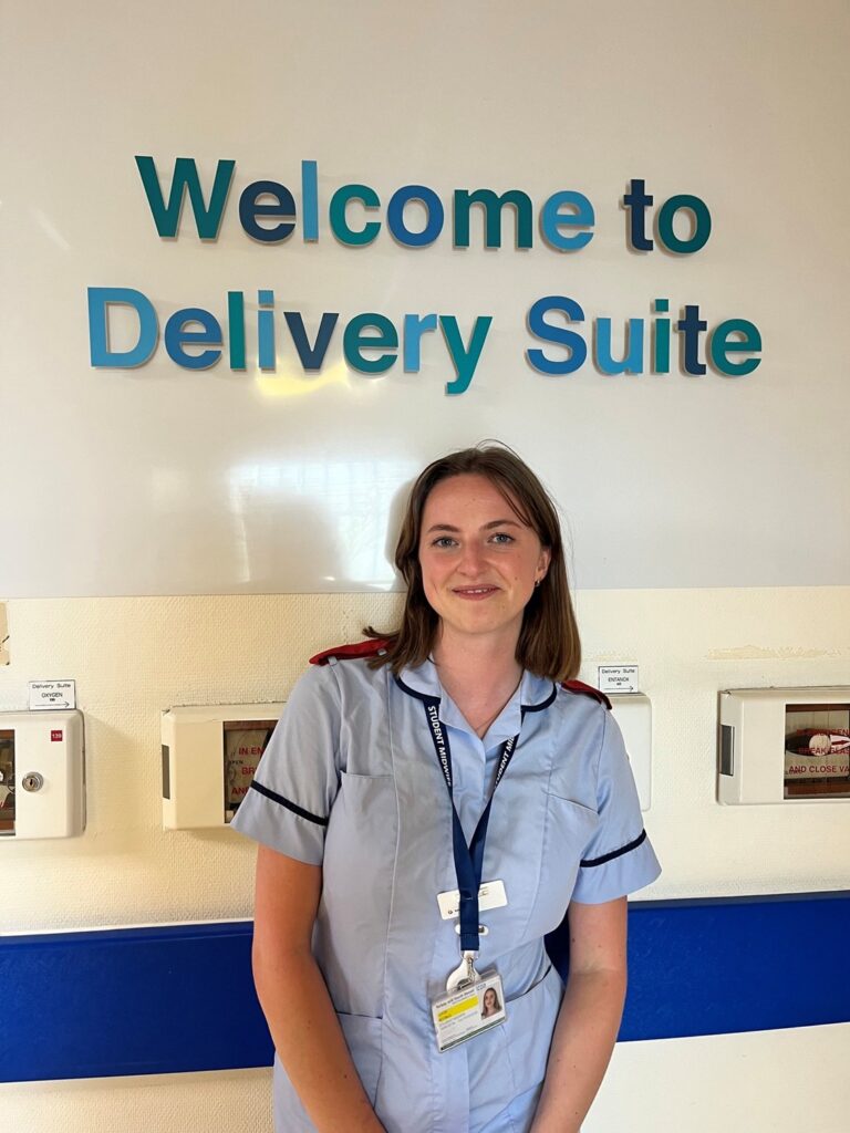 Photo of Lucie Shaw, midwife, by the sign for Torbay Hospital's Delivery Suite