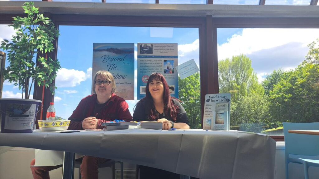 Two people sat at a display stand for Mel Hearn's book launch of Beyond the Rainbow