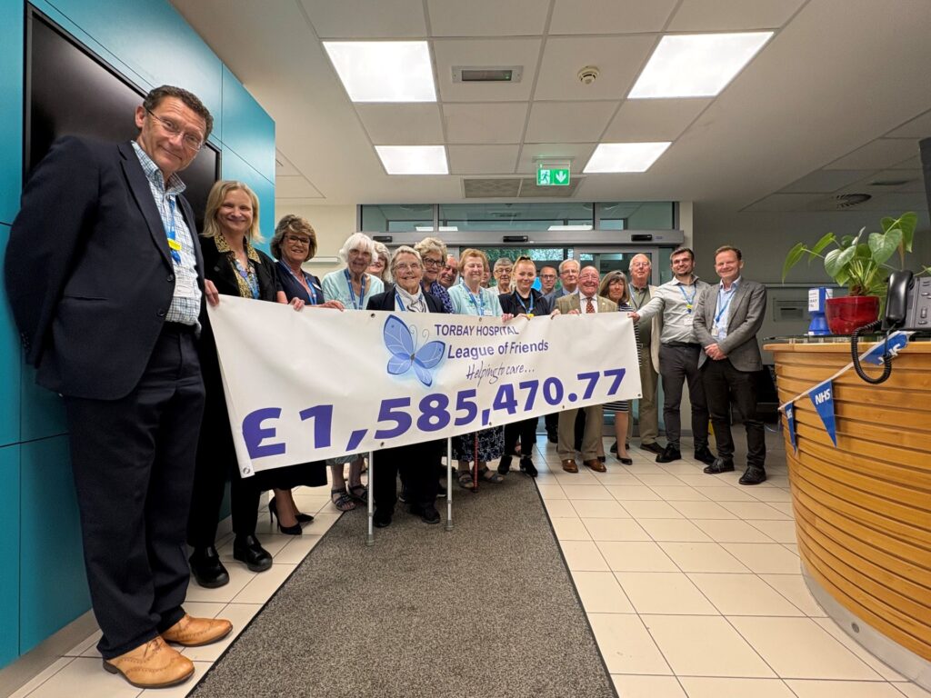 Committee Members of Torbay Hospital League of Friends with Dr Martin Beaman (Chair), Joe Teape (Chief Executive) and representatives from teams at Torbay Hospital holding a large banner printed with the £1,585,470.77 total donated