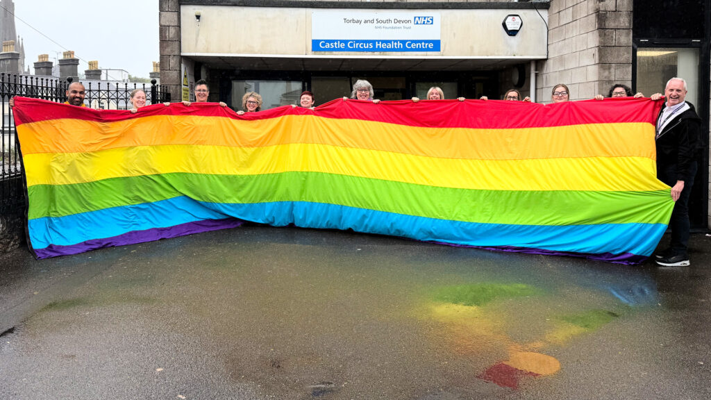 Colleagues holding a large Pride flag outside Castle Circus Health Centre