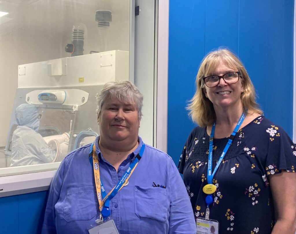Dr Fiona Roberts, Research and Development Director, and Louise Paatz, Accountable Pharmacist for Aseptic Services standing in front of the negative pressure isolator room