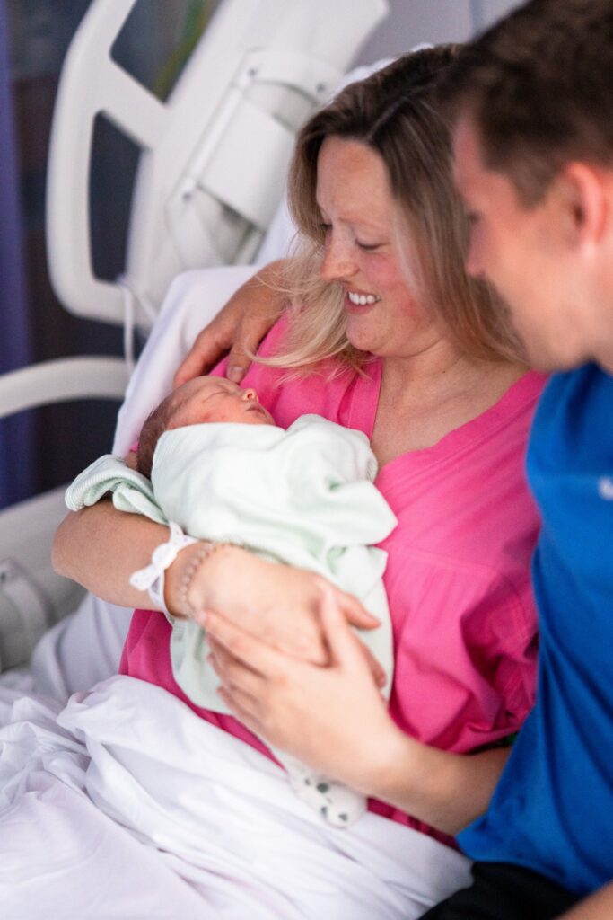 New mum holding her baby, with her partner looking at the baby with his arm around her